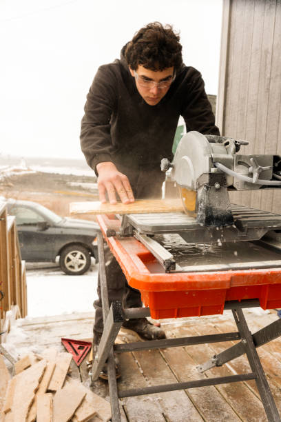Working outside of a house in winter. A construction worker cuts floor tiles.